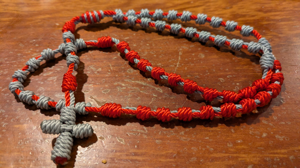 Red and gray cord-knot rosary on a wooden surface