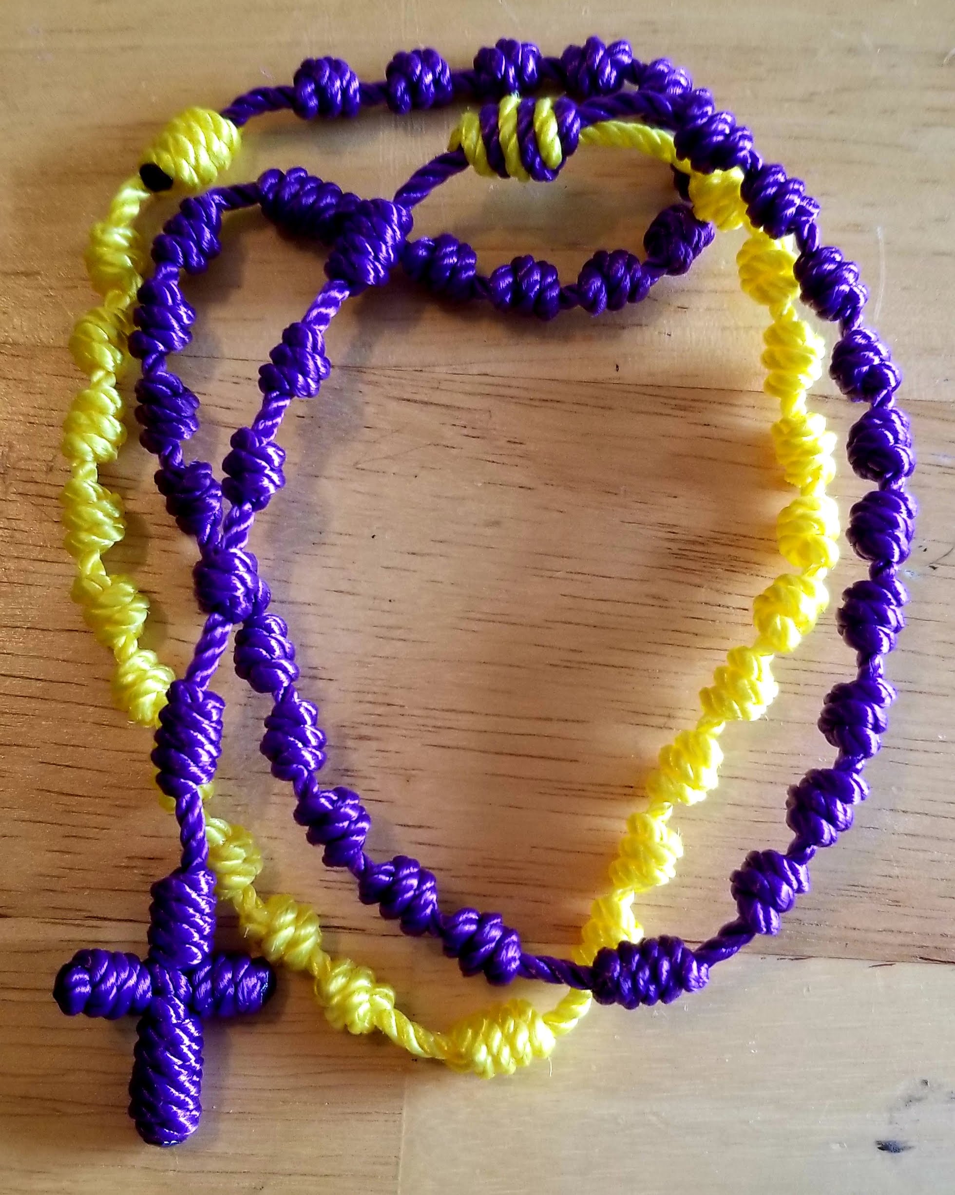 Purple and Yellow cord rosary on a wood background.