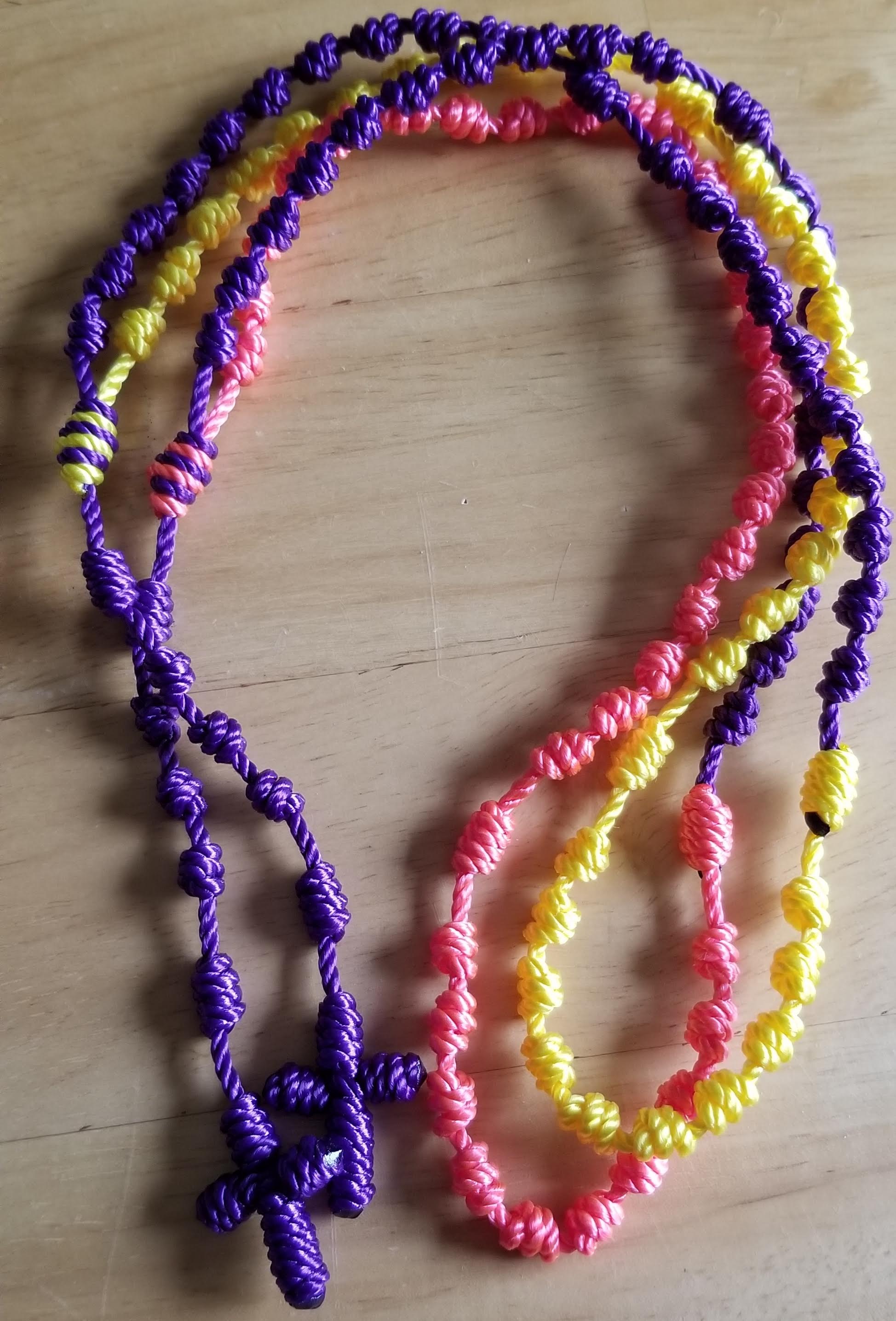 Two rosaries of purple, pink, and yellow on a wood background.
